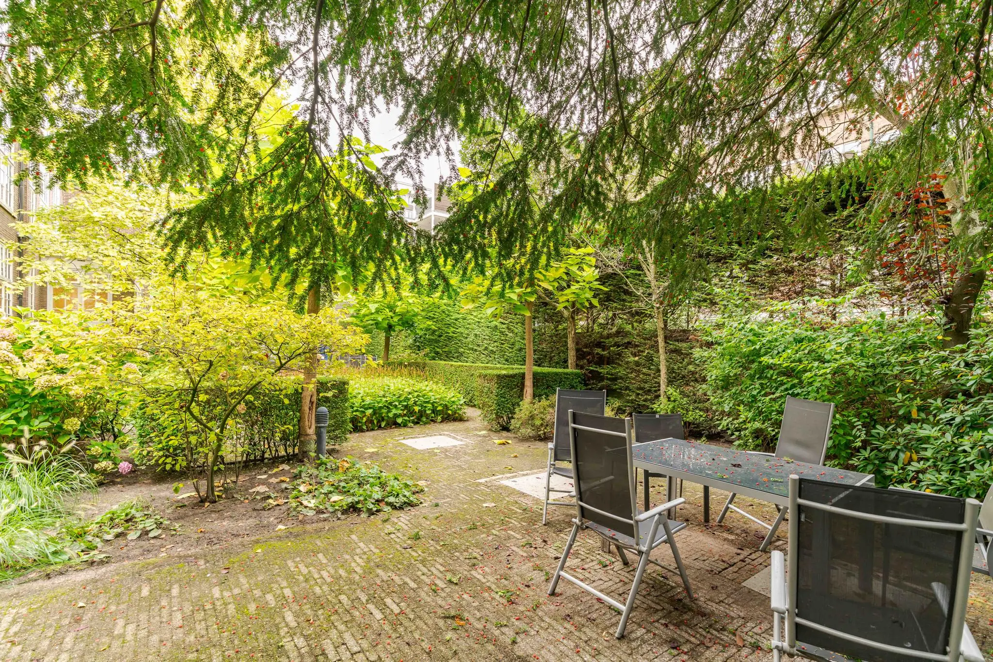 Zicht op een groene, omsloten stadstuin aan het Lange Voorhout met terras en tuintafel met stoelen.